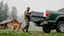 Man loading a truck bed with a dog walking beside him in a foggy outdoor setting.