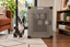 A Boston Terrier sitting on a woven rug beside Impact's gray Stationary Dog Crate in a living room.