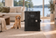 A Golden Retriever sitting on a woven rug beside Impact's black Collapsible Dog Crate in a living room with a lake view.