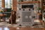 A chocolate Labrador sitting beside Impact's gray Collapsible Dog Crate in a living room.