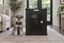 A Miniature Schnauzer sitting beside Impact's black Stationary Dog Crate in a living room.